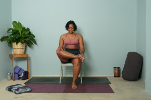 woman sitting on chair with one leg over the other demonstrating a figure 4 pose